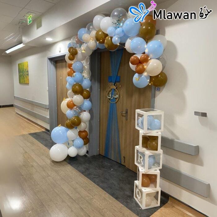 Newborn hospital room setup with balloon arch and baby name boxes