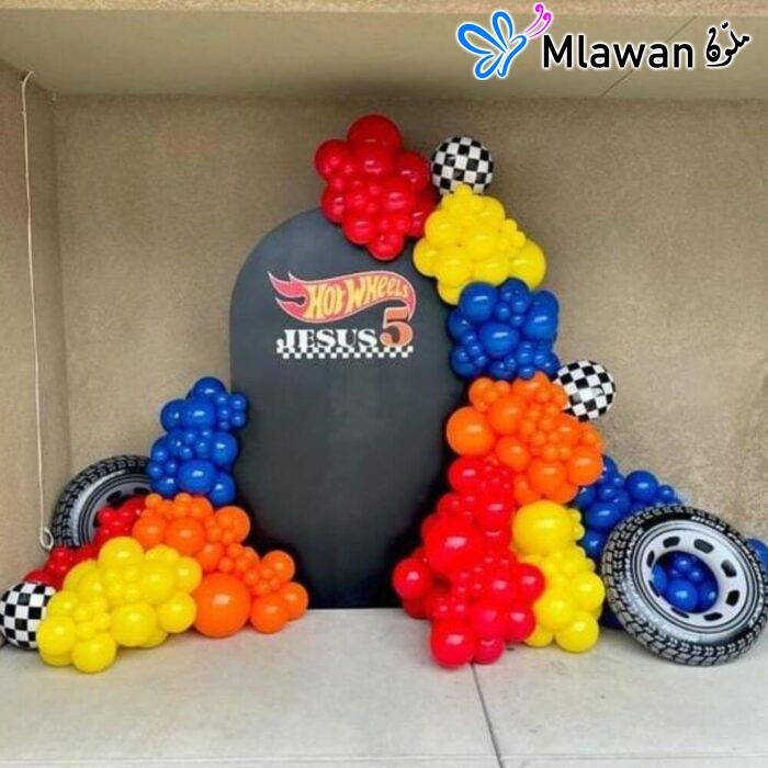 Race car-themed birthday decoration with colorful balloon garland and backdrop.